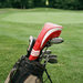 Golf clubs in a bag with a red and white club head cover on a golf course background